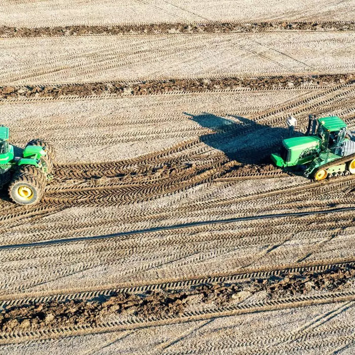 2 John Deere tractors ina field, 1 wheeled and 1 tracked